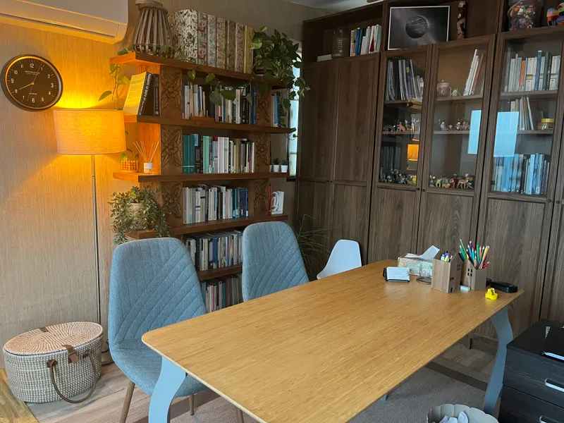 Sala de la consulta, con una mesa de trabajo, sillas y una librería de madera con libros y plantas