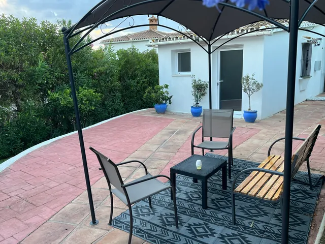 Terraza exterior de la consulta, con mesa y sillas bajo un cenador junto a la fachada blanca del edificio